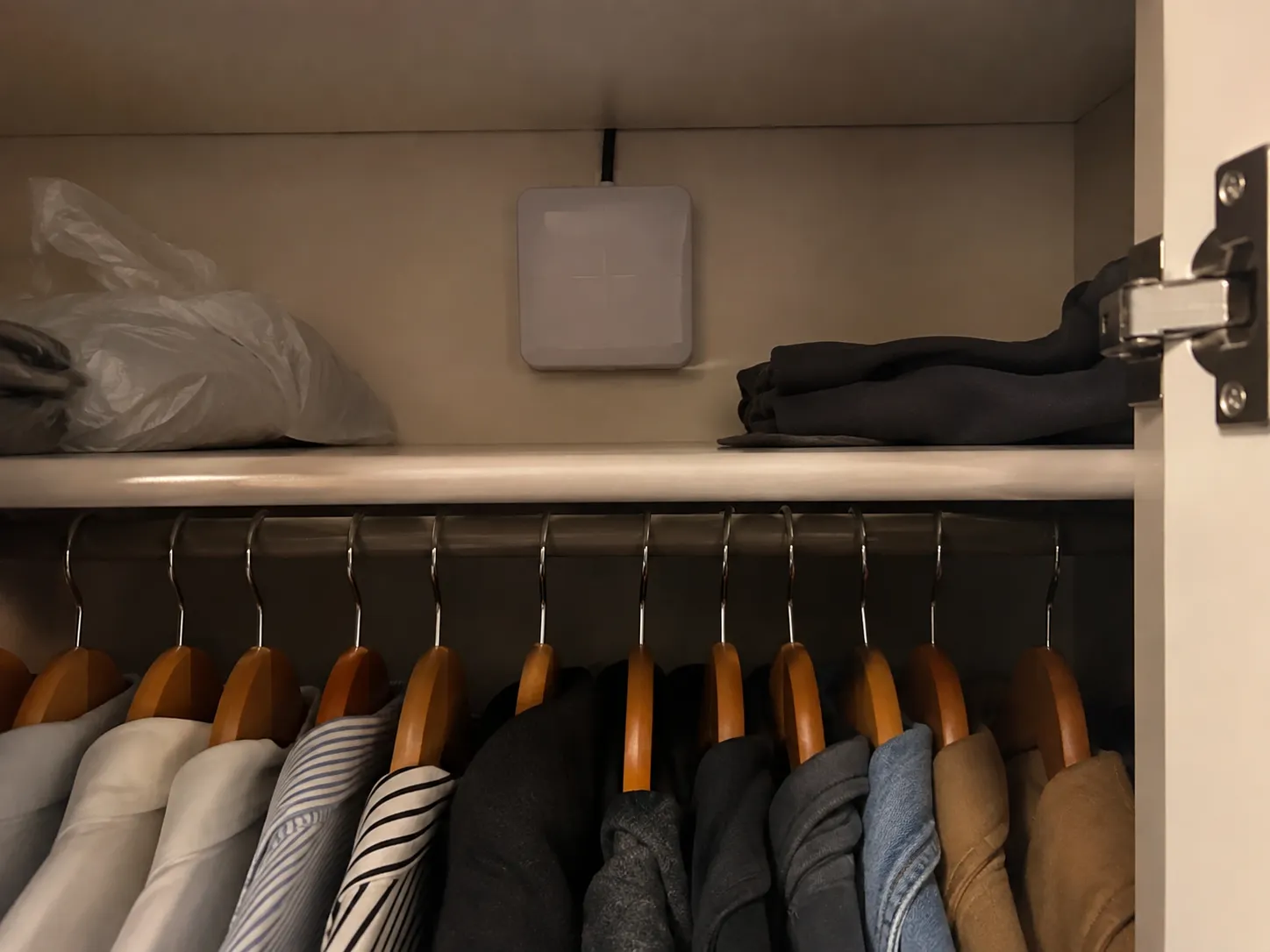 El lector de iCloset instalado en la balda de un armario, junto a ropa doblada y colgada.